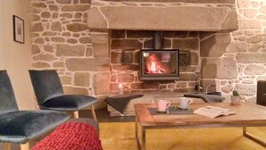 Una chimenea de piedra con fuego, una mesa de madera con un libro y una vela, y dos sillas.