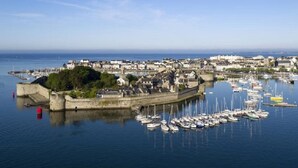 Un pueblo costero con una estructura fortificada, un puerto deportivo con numerosos barcos y una vista despejada del mar.