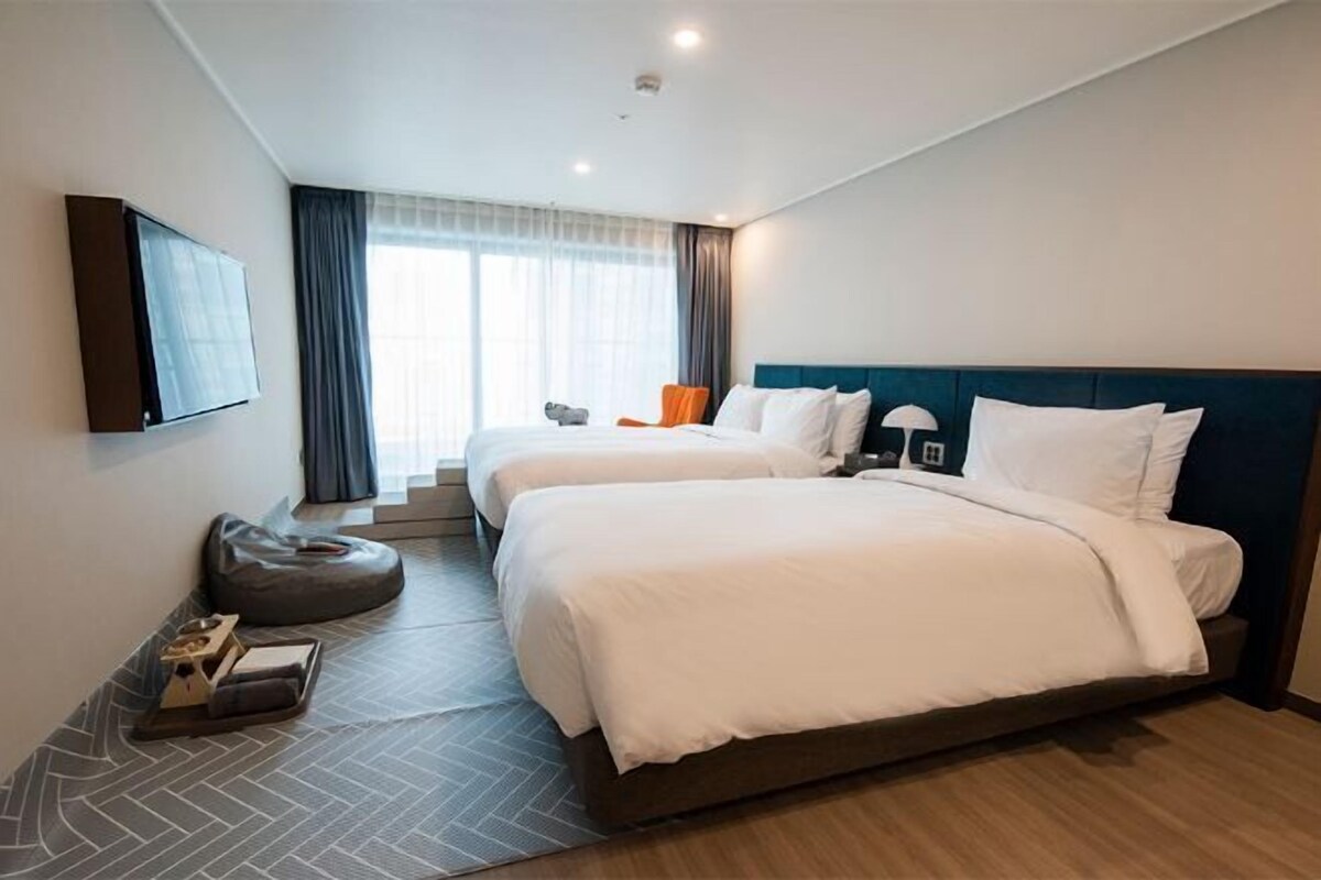 A hotel room with two beds, a flat-screen TV, a sofa, and a small table with a lamp.
