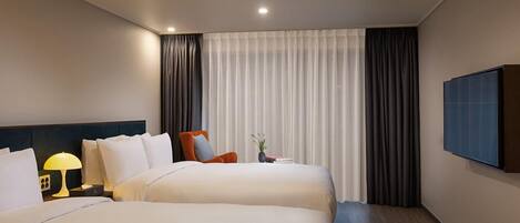 A hotel room with two beds, a nightstand with a lamp, a chair, a small table with a vase, and a TV mounted on the wall.