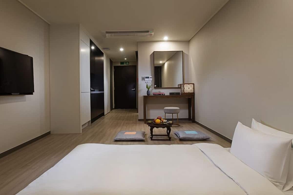 A hotel room with a bed, a desk with a chair, a television, and a mirror.
