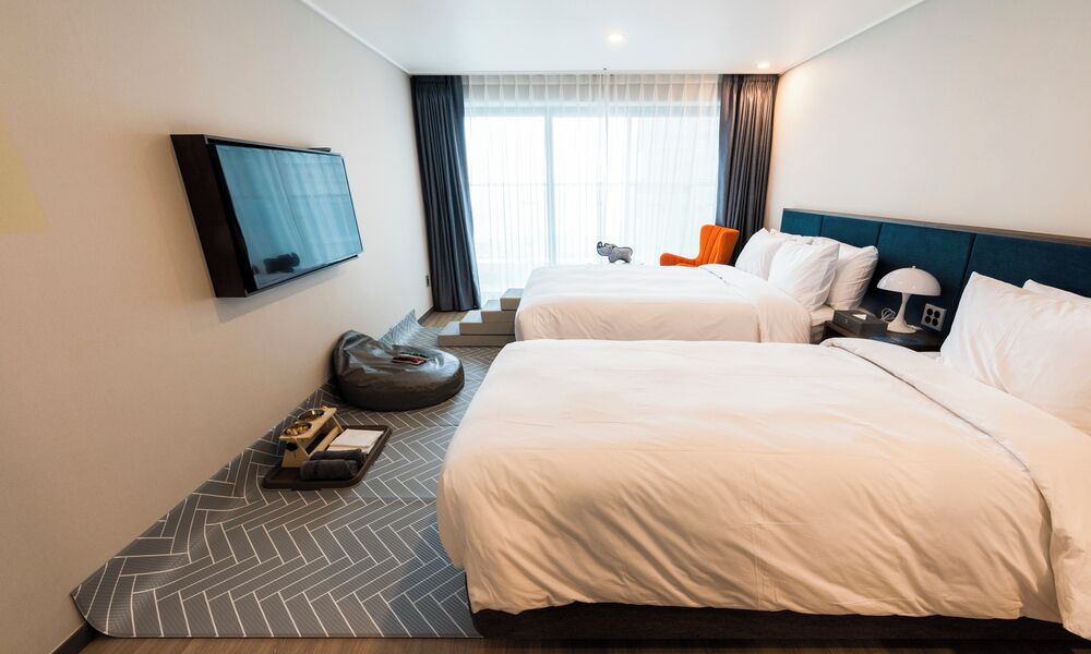 Habitación de hotel con dos camas, televisión, escritorio con lámpara y ventana con cortinas.