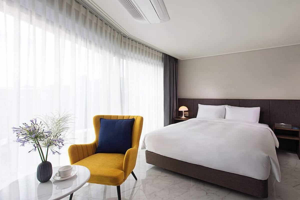 A hotel room with a bed, a chair, a bedside table, and a lamp.