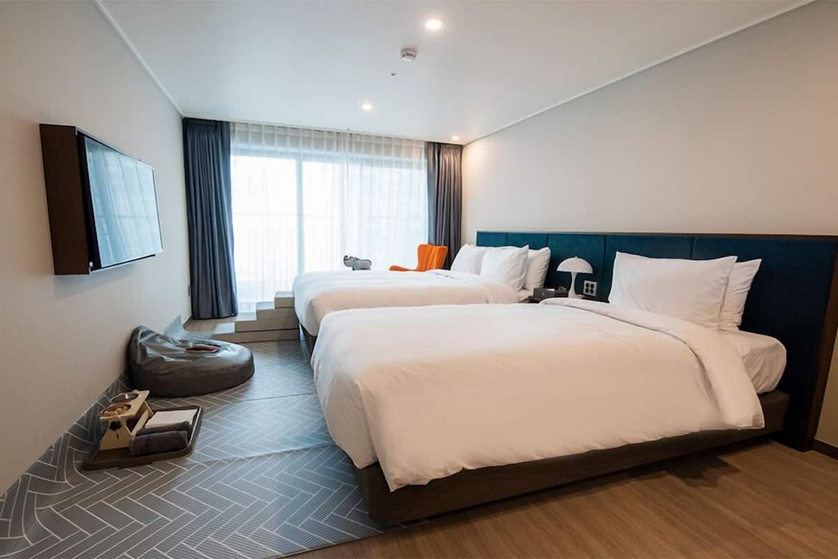 A hotel room with two beds, a TV, a desk, and a chair.