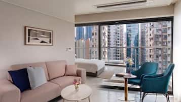 A modern hotel room with a large window, a sofa, a bed, and a small table.