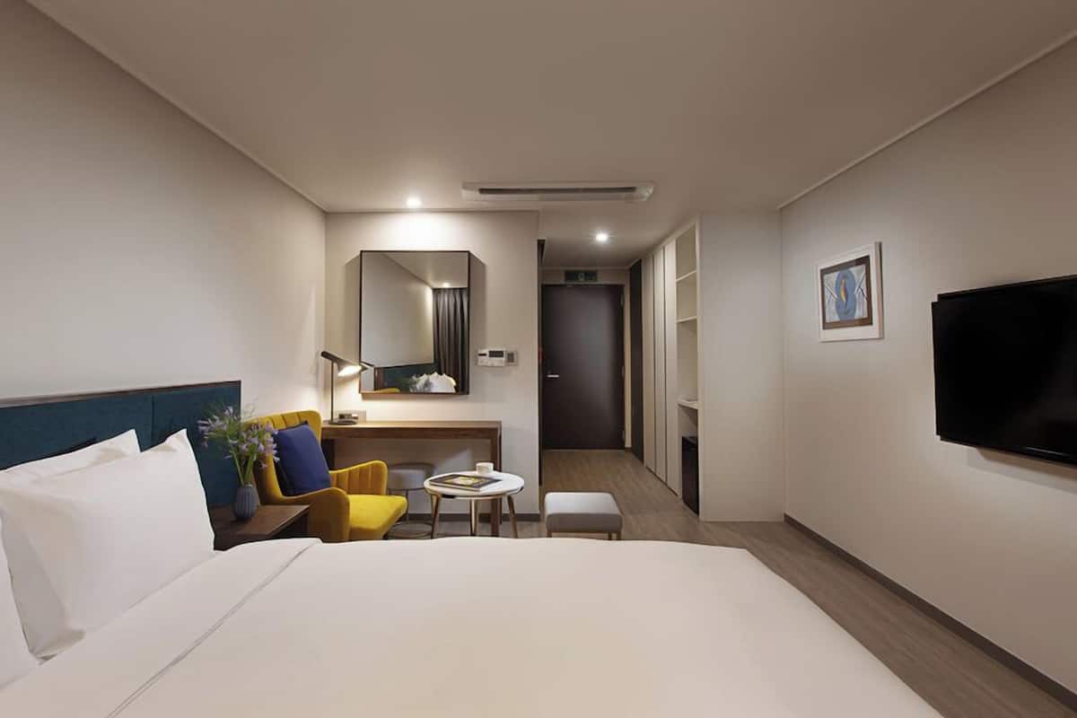 A hotel room with a large bed, a desk, a chair, a small table, a TV, and a mirror.
