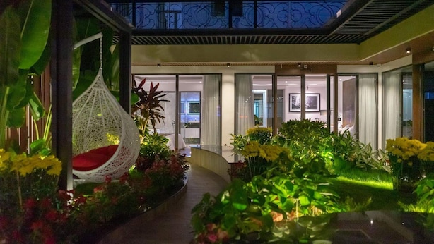 Un espacio exterior moderno con una silla colgante, plantas en macetas y un sendero que lleva a la entrada de un edificio.