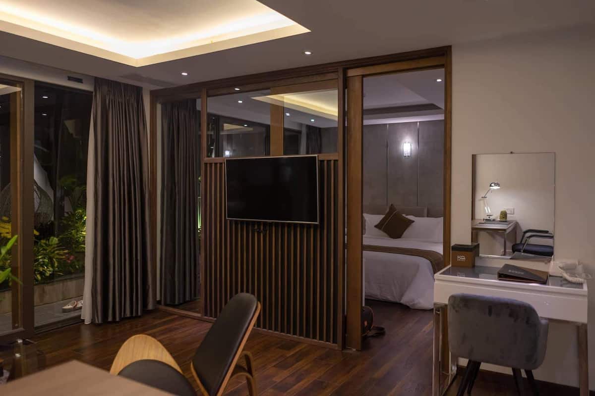 A modern hotel room with a large bed, a desk with a computer, a TV, and a small desk lamp.