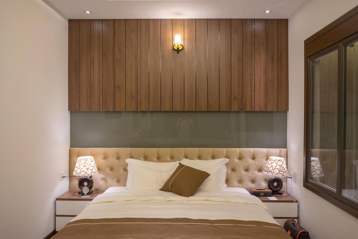 A bedroom with a tufted headboard, two bedside tables with lamps, and a large window.