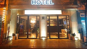 Un hotel con un llamativo letrero que dice 'HOTEL', una entrada a nivel de la calle y un balcón con barandillas.