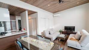 A modern living room with a glass-top dining table, a sofa, and a TV. - BEVERLY HILLS VILLA Miyakojima Resort (Miyakojima)