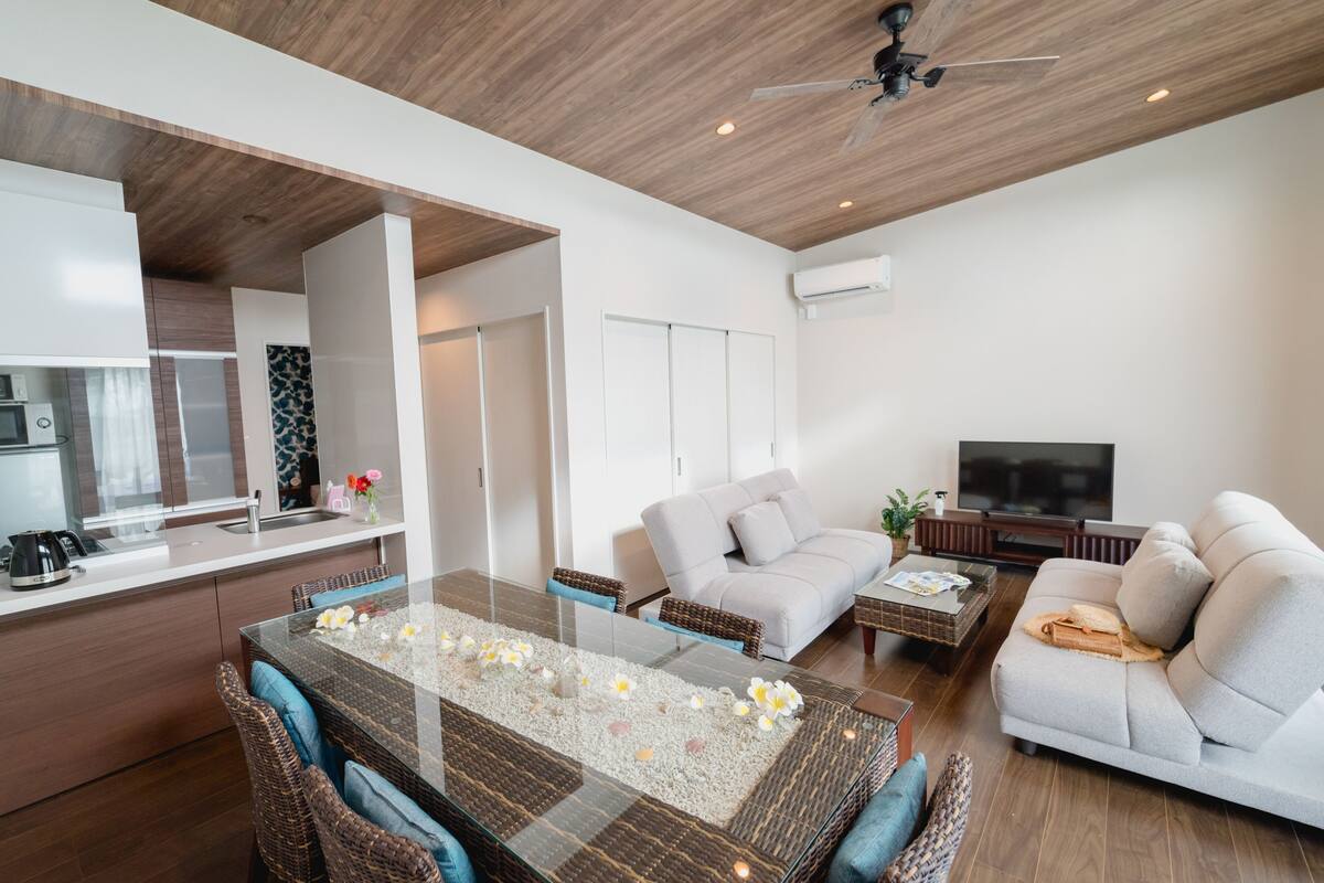 A modern living room with a glass-top dining table, a sofa, and a TV.