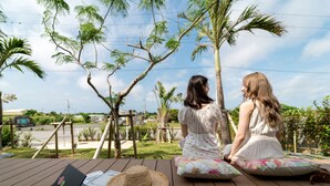 Two people sitting on a wooden deck with a laptop, papers, and a straw hat. - BEVERLY HILLS VILLA Miyakojima Resort (Miyakojima)