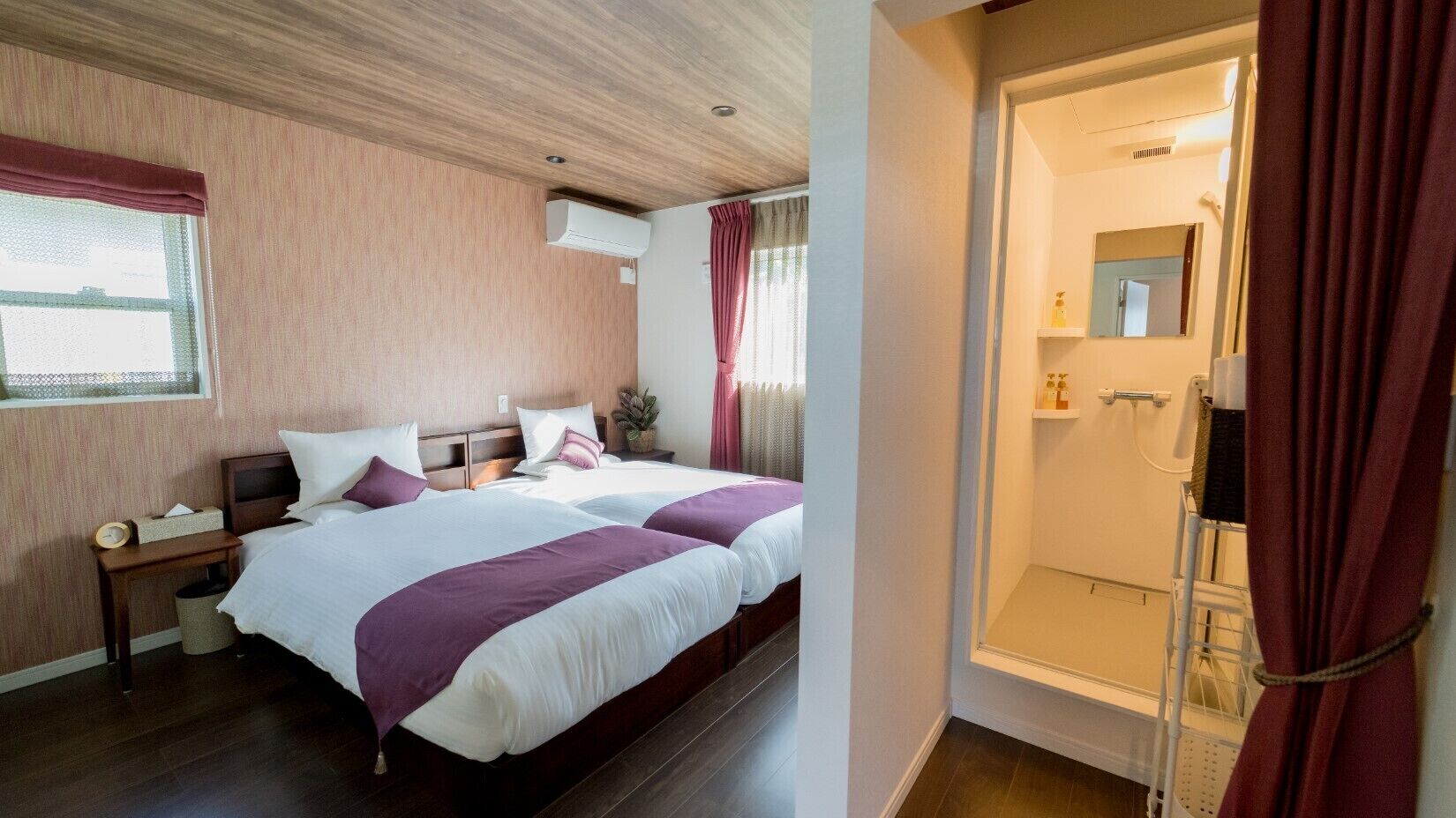 Een hotelkamer met twee bedden, nachtkastjes, een raam met gordijnen en een badkamer met douche.