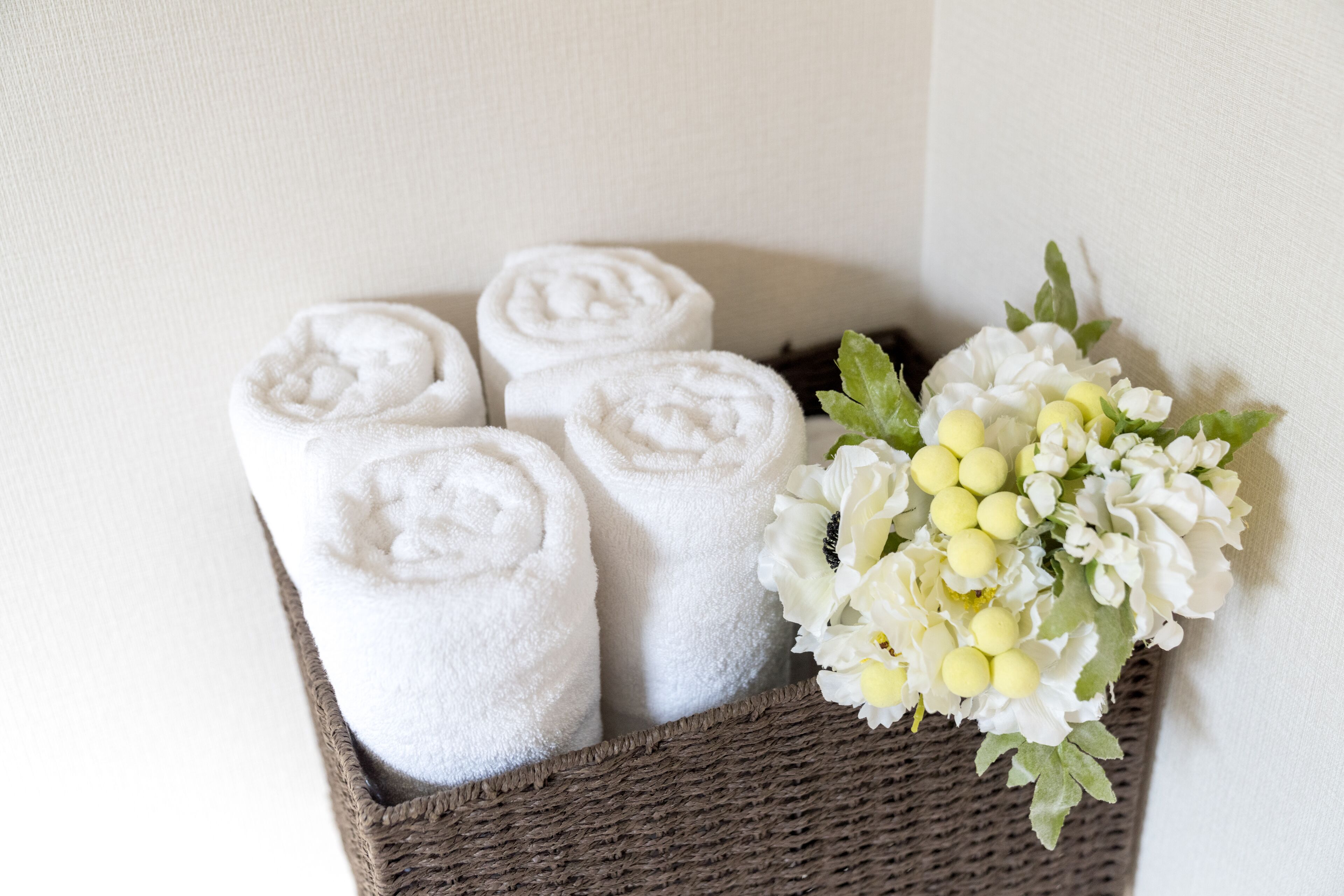 A wicker basket containing rolled white towels and a bouquet of white flowers.