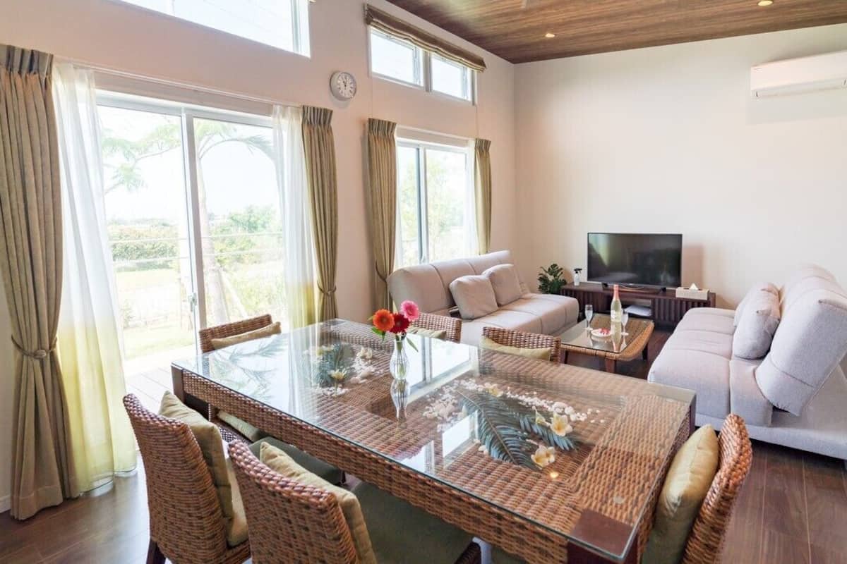 A spacious living room with a glass-top dining table, wicker furniture, a sofa, and a flat-screen TV.