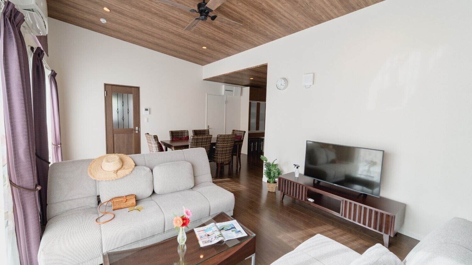 A living room with a sofa, TV, coffee table, and a dining area in the background.