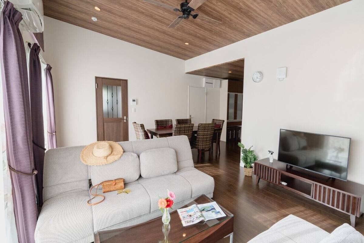 A living room with a sofa, TV, coffee table, and a dining area in the background.