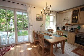 A kitchen with a dining table, chairs, a chandelier, and a view through large windows.
