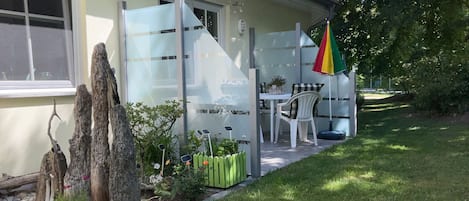 Ein Haus mit einer Terrasse, einem Tisch, Stühlen und einem bunten Sonnenschirm.