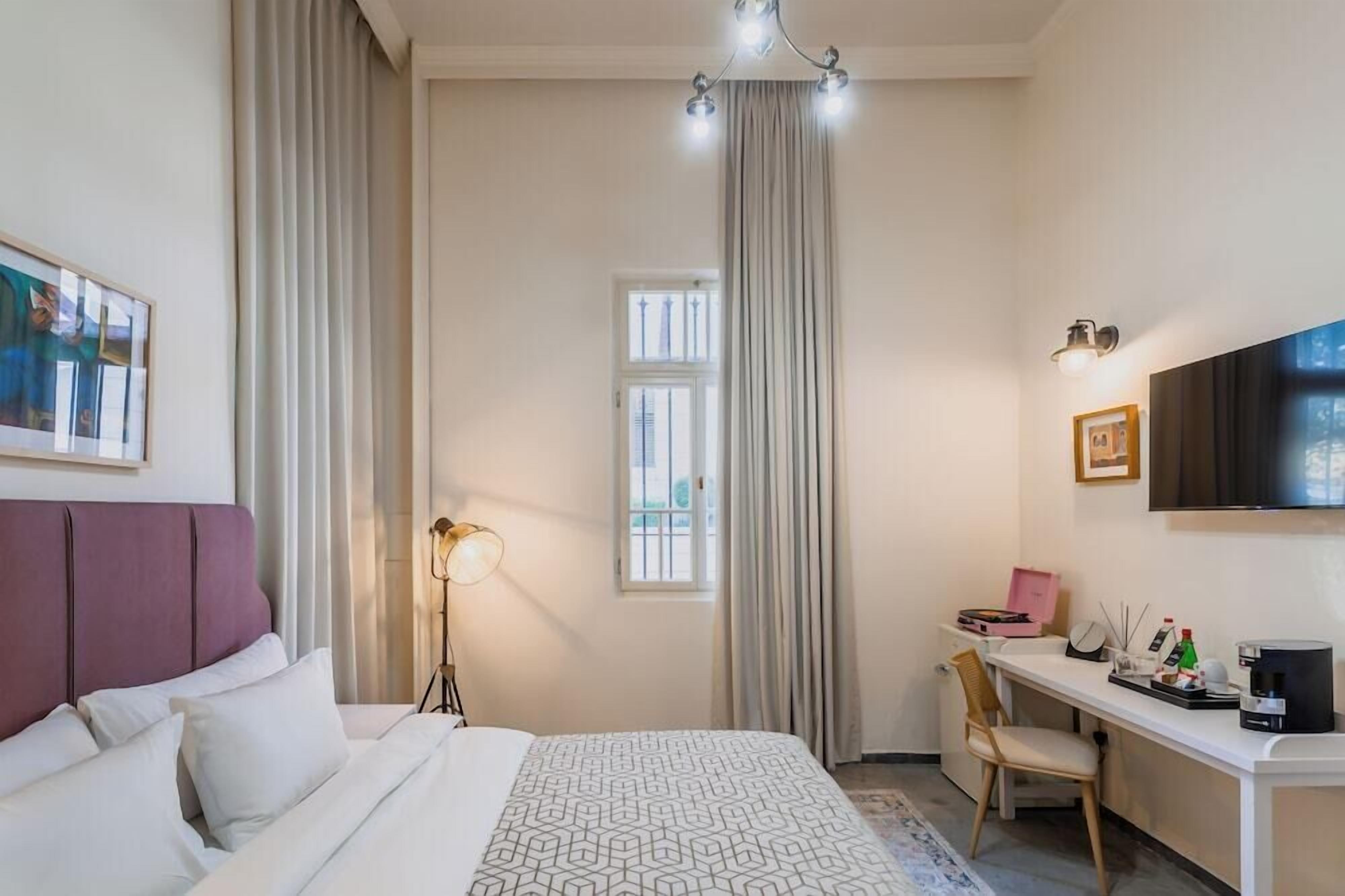 A hotel room with a bed, a desk, a chair, a lamp, a TV, and a window.