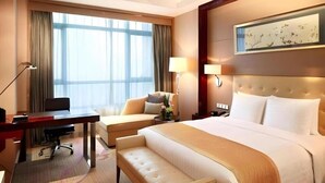 Une chambre d’hôtel avec un grand lit, un bureau, une chaise, un banc, une lampe et un tableau au mur.