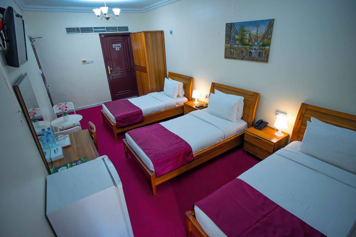 Camera d'albergo con due letti, un armadio in legno, una scrivania con sedia, un tavolino con specchio e un quadro appeso al muro.