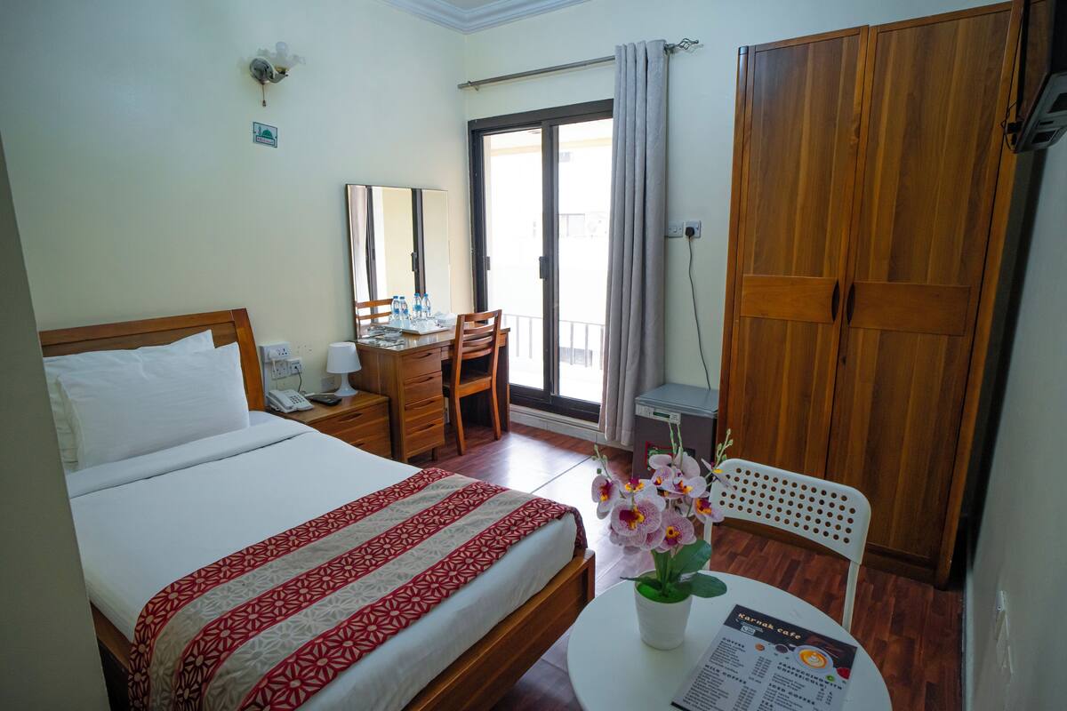 Una camera d'hotel con un letto, una scrivania, una sedia, un armadio e un balcone con vista.