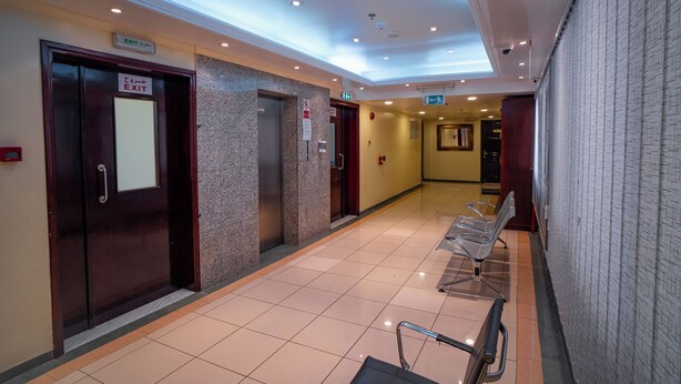 A hotel corridor with an exit sign, a fire alarm, and a waiting area with chairs. - Al Karnak Hotel (Dubai)