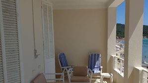 Een balkon met wit meubilair, waaronder stoelen en een tafel, met uitzicht op een strand.