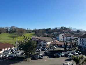 A parking lot with cars, a building with a red roof, and a green field in the background. - Apartment in Ciboure with heated pool and private parking (Ciboure)
