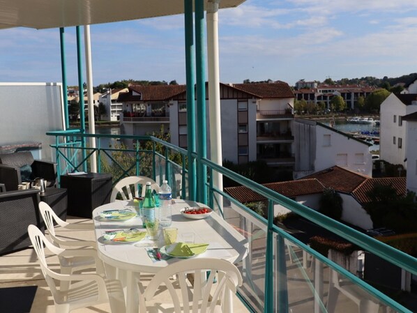 A balcony with a table set for dining, overlooking a residential area with buildings and a body of water. - Apartment in Ciboure with heated pool and private parking (Ciboure)