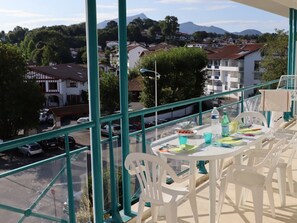A balcony with a table and chairs, overlooking a street with parked cars and buildings. - Apartment in Ciboure with heated pool and private parking (Ciboure)