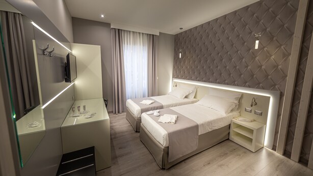 A modern hotel room with two beds, a large mirror, a vanity with a mirror, and a bedside table with a phone.