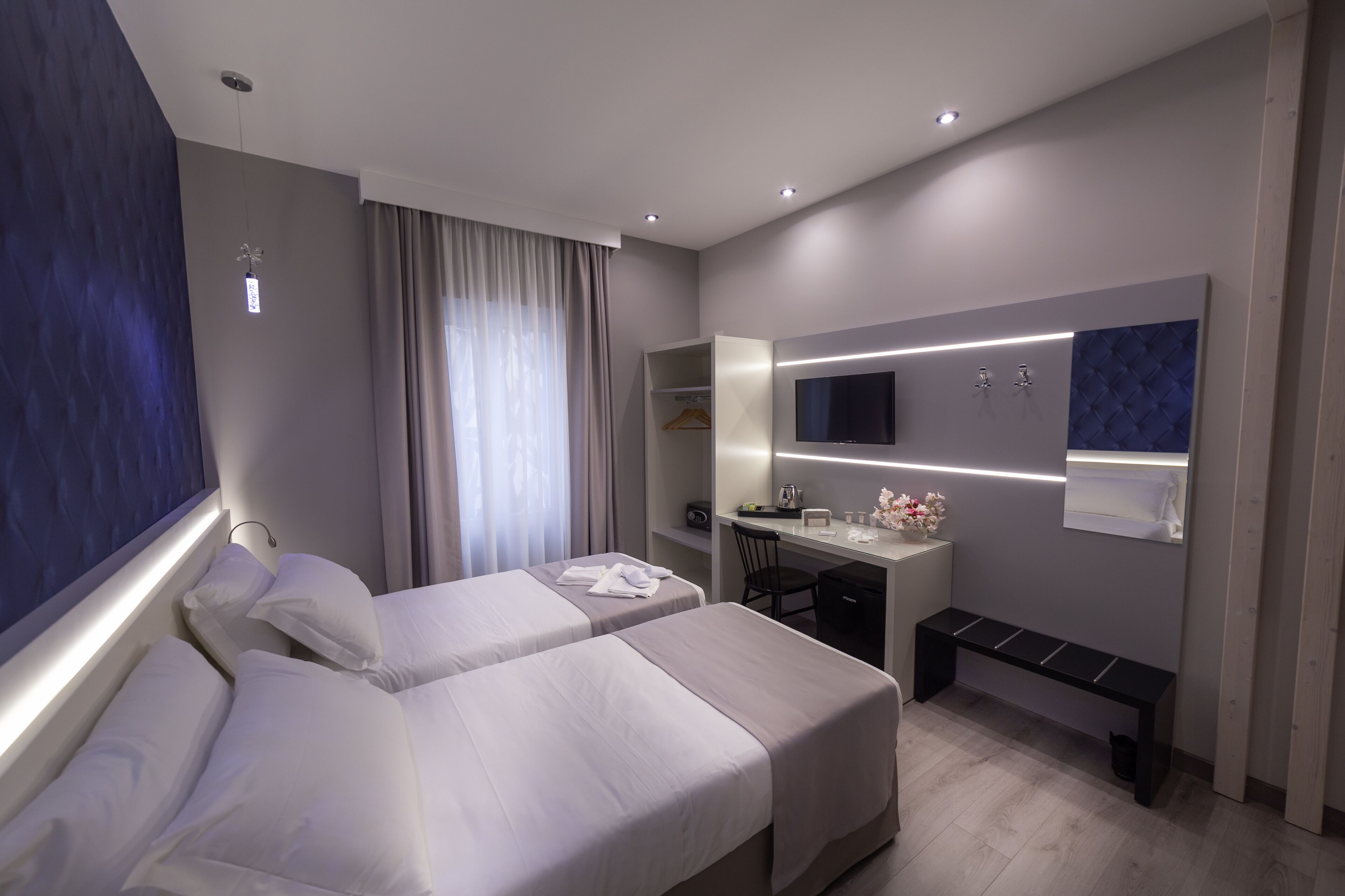 Camera d'albergo moderna con due letti, una scrivania, una sedia, una panca, uno specchio e una TV.