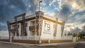 A modern hotel with a prominent 'HOLYGOLD' sign, featuring a symmetrical facade with decorative metal panels and a flat roof.