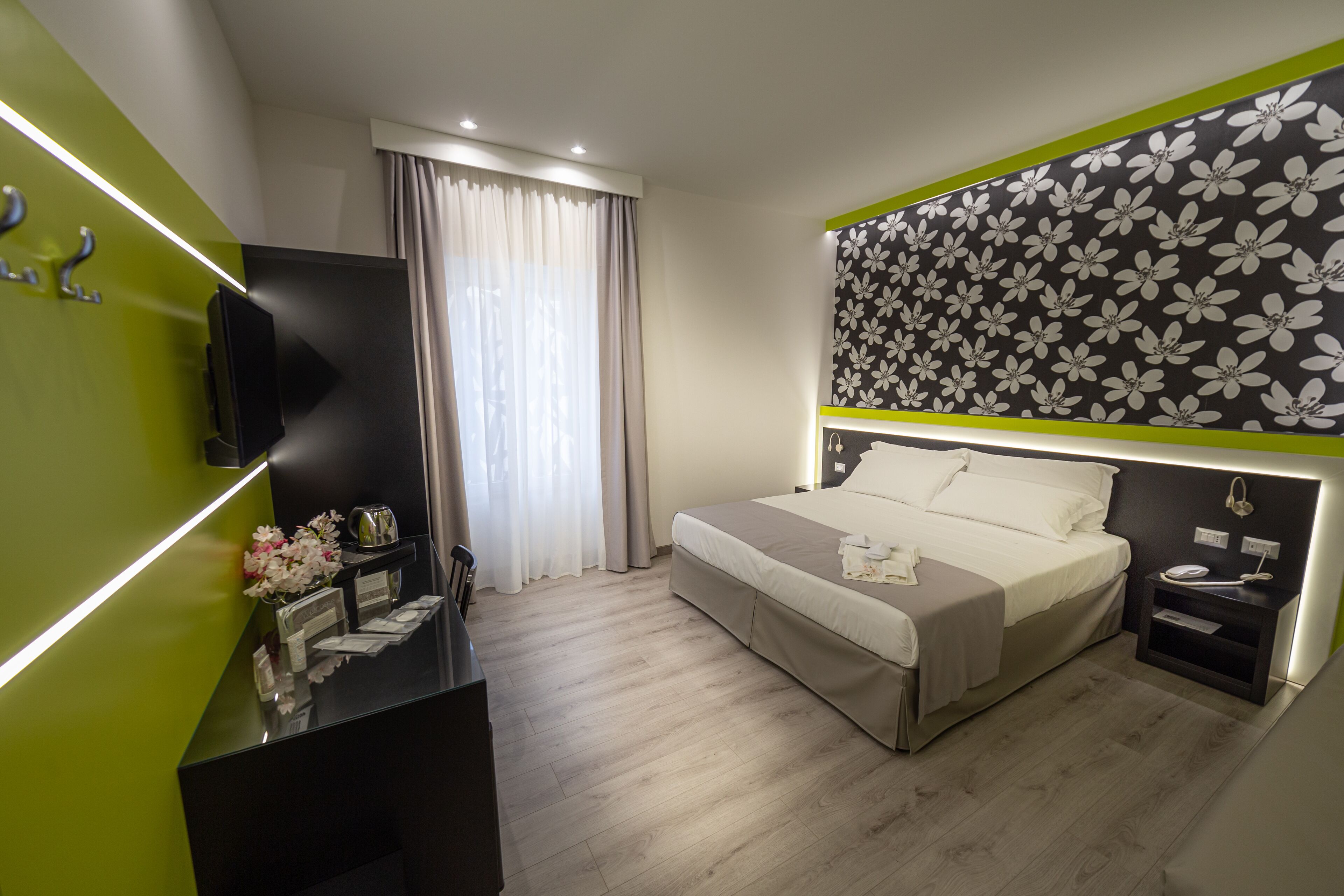 Une chambre d’hôtel moderne dotée d’un grand lit, d’un bureau avec un téléviseur à écran plat, d’une table de chevet et d’un arrangement floral.