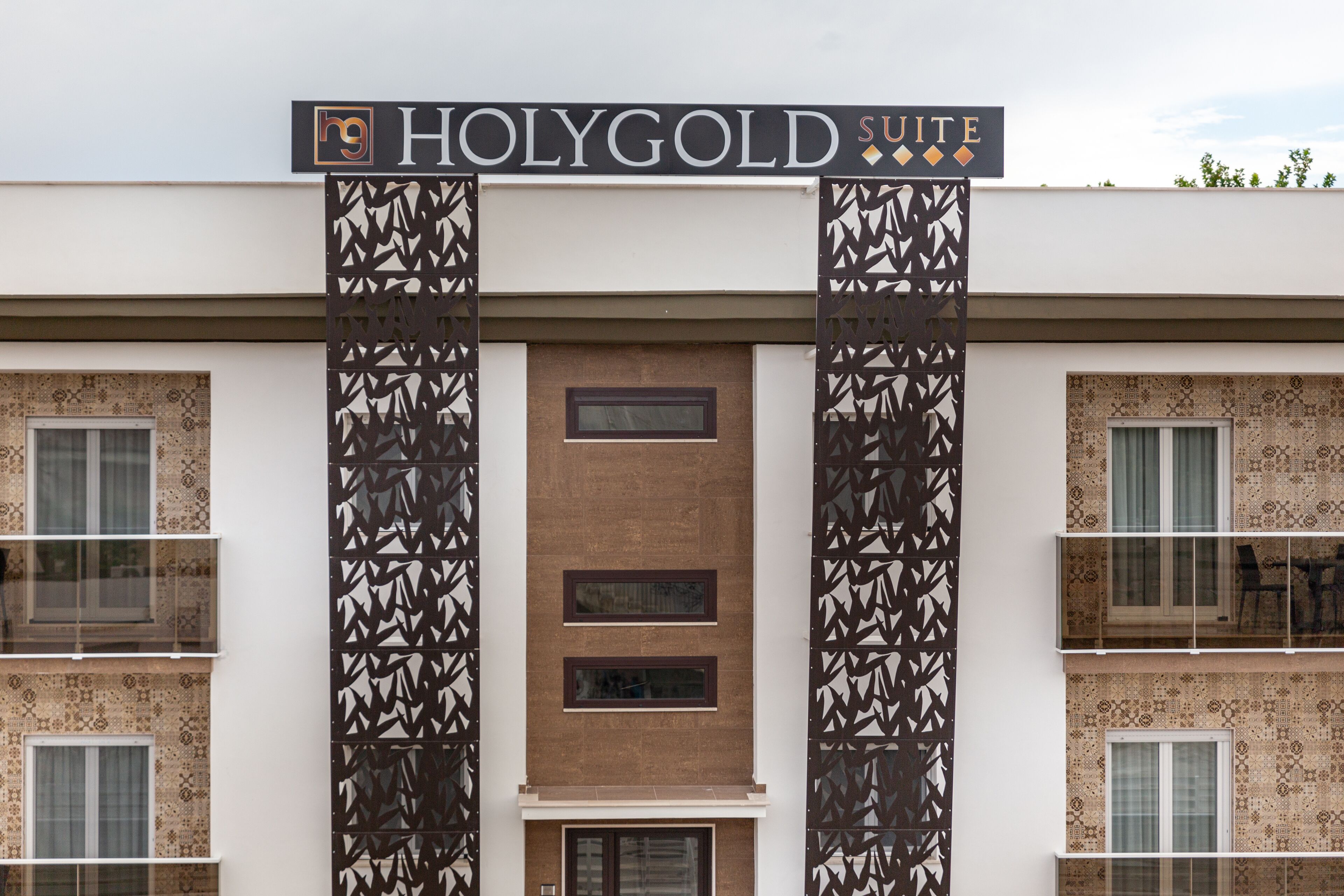 Hotellin sisäänkäynti, jonka yläpuolella on kyltti, jossa lukee: ”HOLYGOLD SUITE”.