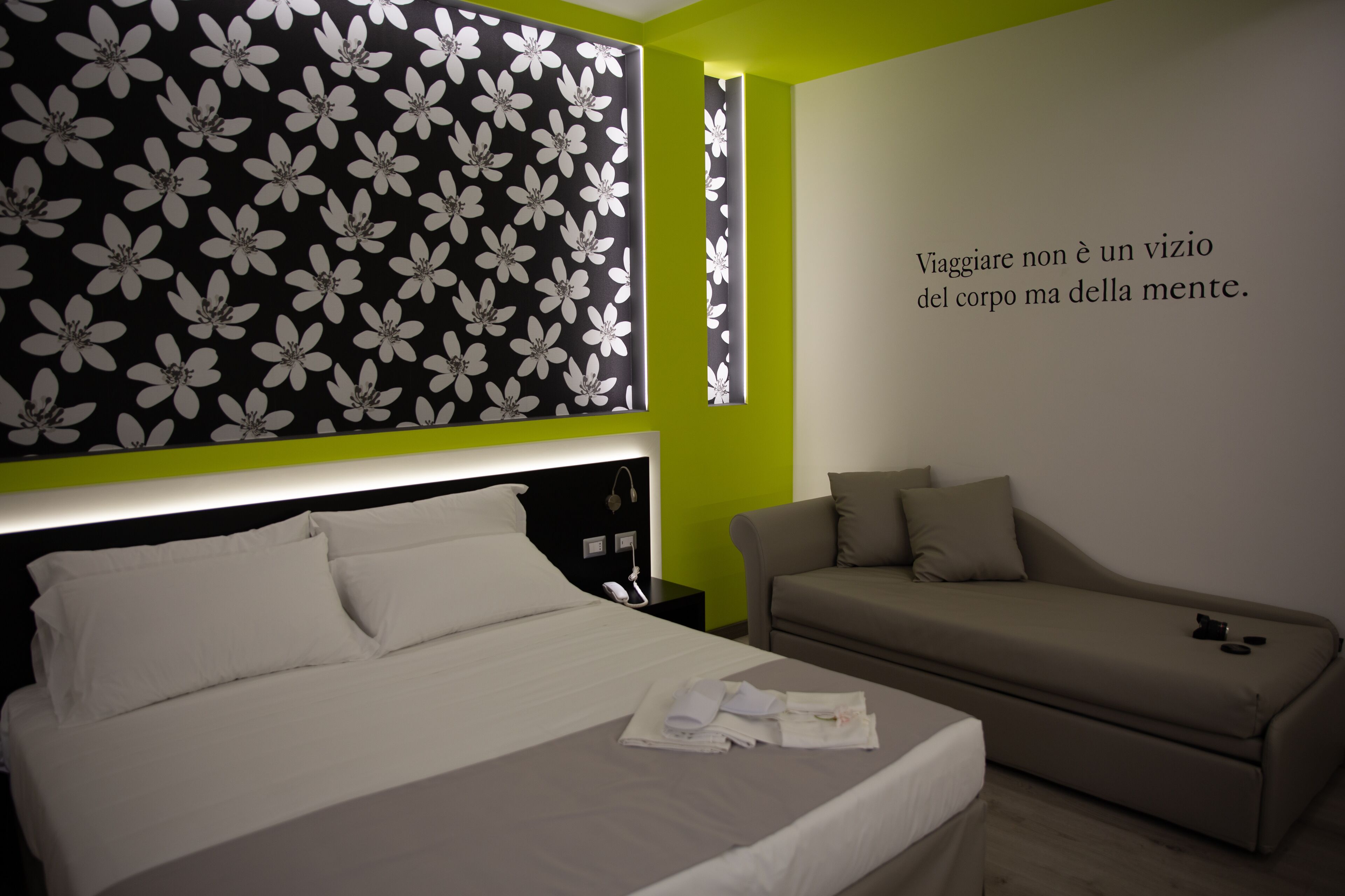 A hotel room with a bed, a sofa, a wall with a floral pattern, and a motivational quote.