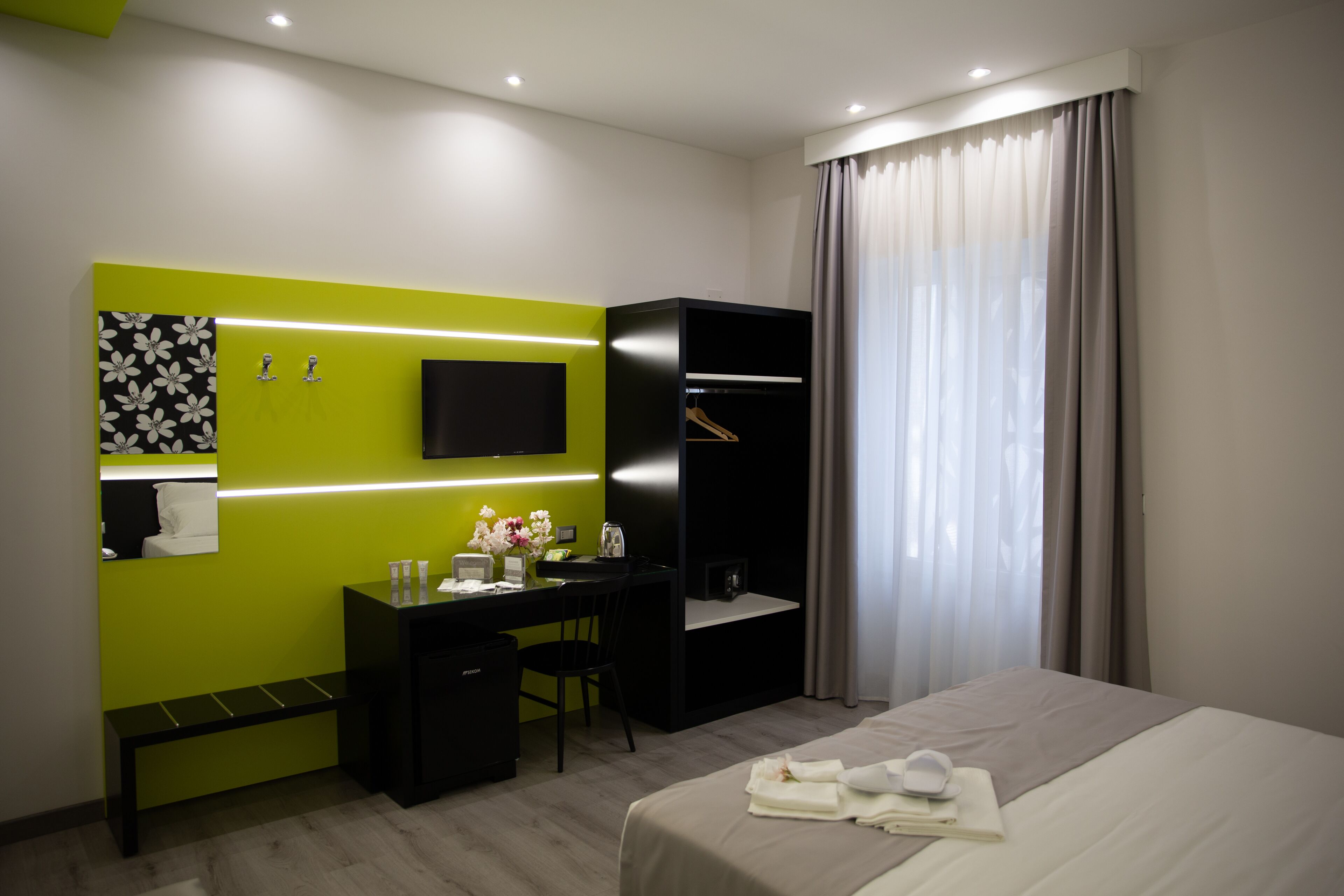 Een moderne hotelkamer met een bed, een bureau, een stoel, een televisie en een kledingkast.