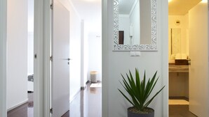 A hallway with a potted plant, a decorative mirror, and a door leading to a bathroom. - Design Gardens, a Home in Madeira (Funchal)