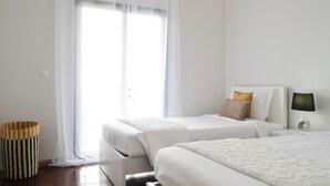 A hotel room with two beds, a bedside lamp, a small side table, and a wicker basket. - Design Gardens, a Home in Madeira (Funchal)