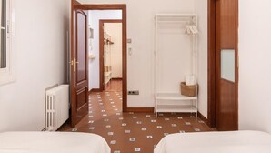 Una camera d'albergo con due letti, un termosifone, un armadio, uno scaffale con asciugamani e una porta che dà su un'altra stanza.
