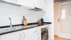 Een moderne keuken met witte kastjes, een roestvrijstalen spoelbak, een houten snijplank en een koffiezetapparaat.