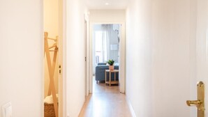 Een smalle gang met een houten vloer die leidt naar een woonruimte met een bank en een kleine tafel met een plant.