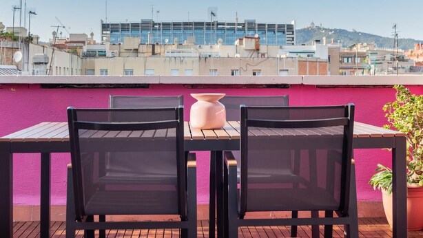 Een terras op het dak met een tafel, stoelen, een bloempot en uitzicht op de stad.