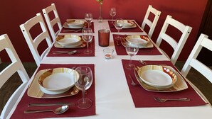 Una tavola da pranzo imbandita per quattro, con sedie bianche, sottopiatti rossi e piatti con bordo dorato.