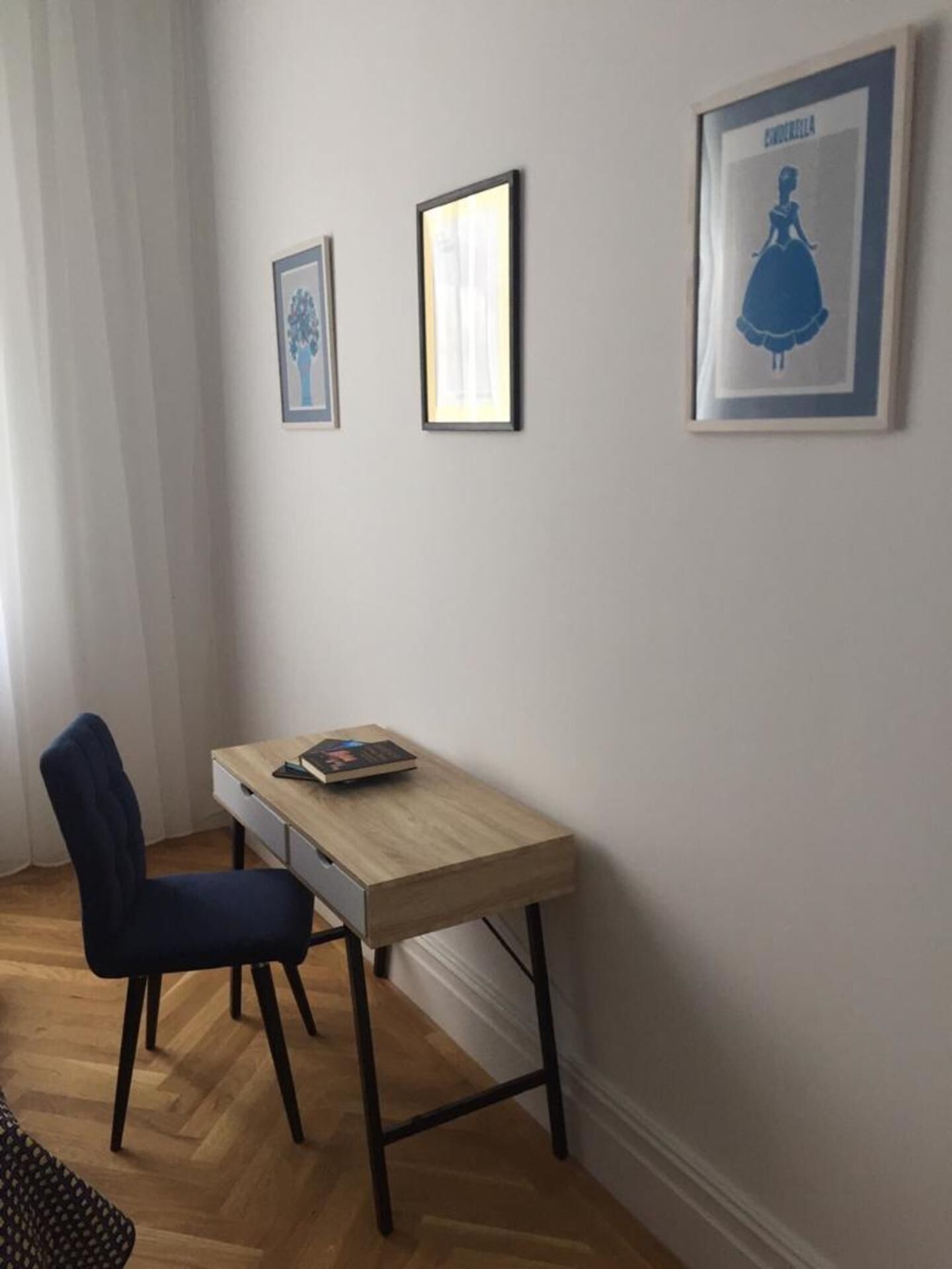 Una habitació petita amb un escriptori de fusta, una cadira i dos quadres penjats a la paret.