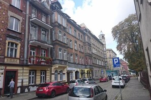 A street view with multi-story buildings, parked cars, and a blue parking sign.
