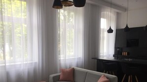 Ein modernes Wohnzimmer mit einem grauen Sofa, zwei runden Beistelltischen und einer Küchenzeile mit schwarzer Arbeitsplatte und Edelstahlgeräten.